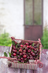 rzd fresh cherry with leaves on cardboard box in red and white fabric,on old garden housse doord background. view, copy space
