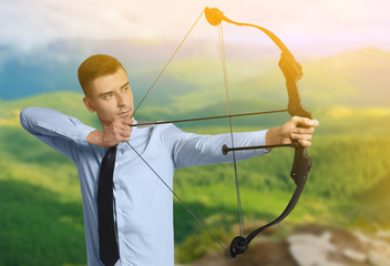 Young businessman practicing archery on grey background