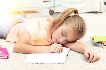 Attractive tired little girl lying on the floor with copybook