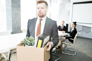 Fototapeta na wymiar Waist up portrait of bearded young man holding box of personal belongings and leaving office after being fired from job