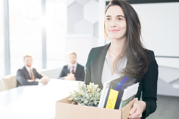 Waist up portrait of smiling young businesswoman holding box of personal belongings  leaving office after quitting job, copy space