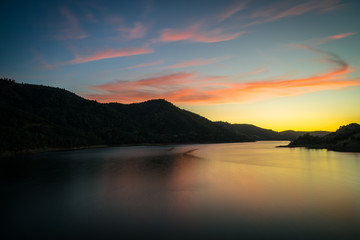 Fototapeta na wymiar Smooth Water of Don Pedro Reservoir, With Pink Sunset Clouds