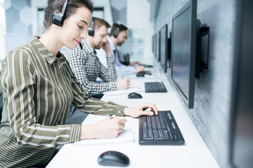 Side view portrait of smiling young woman  wearing headset  working with group of help desk...