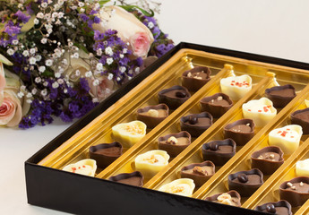 A box of fancy chocolates next to a bouquet of pink roses. Gifts for special occasions