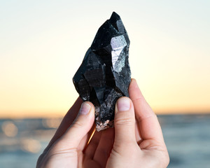 Woman holding Morion Smokey Quartz with Chlorite  in her hand at sunrise in front of the lake.