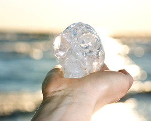 Woman's hand holding Quartz Carved Elongated Mayan Alien Crystal Skull at the sunrise in front of the lake.