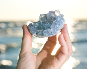 Blue Celestite cluster from Madagascar in woman's hand at sunrise in front of  the lake.