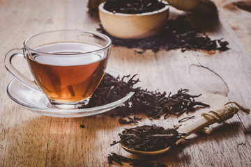 close-up dry chinese tea in wooden spoon on table, a cup of tea on saucer background, vintage tone