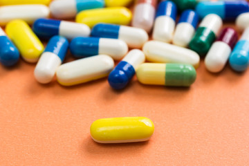 Heap of assorted colorful capsules on orange background. One yellow pill is apart, isolated.