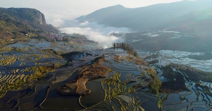 Drone flight over water-filled rice terraces towards a valley covered with dynamic mist. Yuanyang Rice Terraces early in the morning during spring. Part 1 of 4, can be merged to a continuous movie.