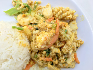 Stir-fried seafood, prawn and squid with yellow curry powder with rice and fried egg in white plate on white background. Thai style food.
