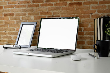 Office desk with blank screen laptop and blank poster.