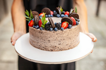 The girl is holding a cake with forest berries, strawberries, blueberries, on the street in the city. A concept for the production of cakes, bakeries, restaurants. Background image