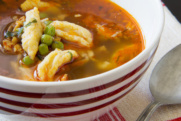 Bowl of Romanian chicken and dumpling soup with peas on a linen red striped tablecloth napkin