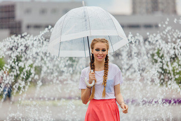 Young pretty girl with two braids in yellow boots and with transparent umbrella stands near...
