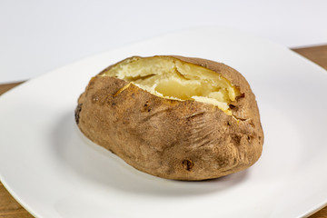 Fully loaded baked potato on a white plate on the kitchen table