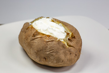 Fully loaded baked potato on a white plate on the kitchen table