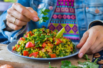 Woman hands adds parsley to Tabbouleh. Levantine vegetarian salad with parsley tomatoes, mint, onion, bulgur, couscous. Vegan Arabian or Israeli traditional food served as part of meze