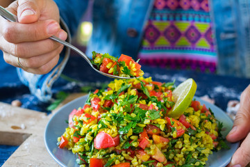 Woman hands holds Tabbouleh. Levantine vegetarian salad with parsley, tomatoes, bulgur, couscous, olive oil, lemon juice. Vegan Arabian or Israeli traditional food served as part of meze