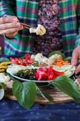Woman hands holds cauliflower with chopsticks. Eating vegan Buddha Bowl dish. Vegetables. Carrot, seaweed, onion, tomato, cucumbers, tomato sauce, sesame seeds. Raw vegan vegetarian food