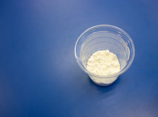 All purpose flour in clear plastic cup isolated on blue background. Ingredient for making play dough in science experiment.