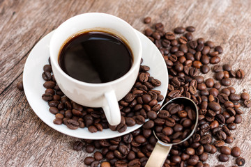 Hot coffee in white cup with coffee beans on wooden table with copy space.
