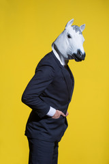 A man in a suit and a horse mask on a yellow background. Conceptual business background