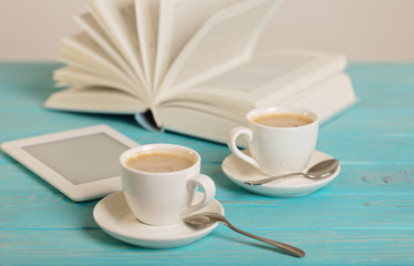 Book, e-book and two white cups of coffee on a wooden blue background.