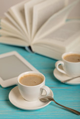 Book, e-book and two white cups of coffee on a wooden blue background.