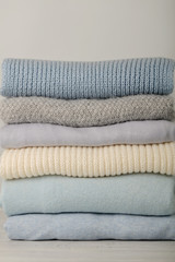 Pile of knitted clothes (sweaters, scarves, pullovers) blue, white and grey colors.