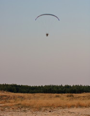 Fototapeta Motolotniarz w powietrzu, na ziemi piaszczysty teren, suche trawy i linia lasu obraz