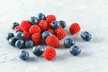 Blueberries and raspberries on the background of gray cement. Ripe and juicy fresh raspberries and blueberries close-up. A lot of berries close-up.