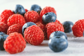 Blueberries and raspberries mix on the background of gray cement. Ripe and juicy fresh raspberries and blueberries close-up. A lot of berries close-up.