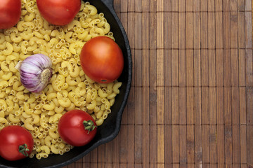 raw pasta and tomatoes in a frying pan, salt and spices on a background of a bamboo napkin.