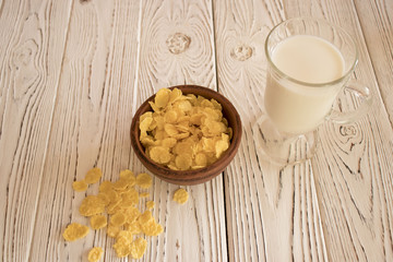 Delicious corn flakes in a clay bowl with a glass of milk. Rustic wood background. Healthy crispy snack for Breakfast.