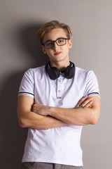 Handsome boy teenager with headphones stands with crossed arms near wall in grey studio