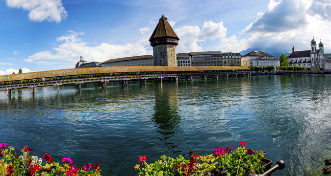 A fantastic panoramic view of the historical wooden bridge - Chapel Bridge, across River Reuss -  Lucerne. The water tower & other heritage buildings along with the flowers add a unique charm.