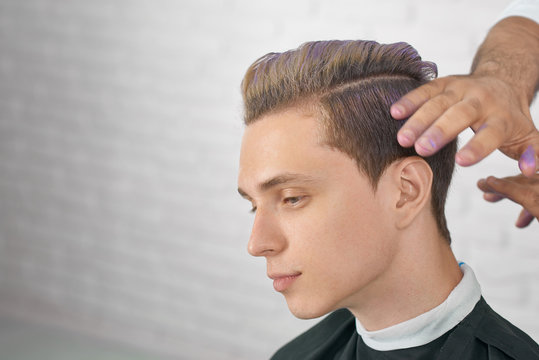 Young male model waiting for new hairstyle with lilac hair coloring.  Hairdresser's hands doing stylish coloring for handsome boy. Working on  white brick studio background. Stock Photo | Adobe Stock
