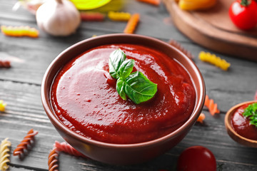 Bowl with tasty tomato sauce on wooden table, closeup