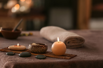 Burning candles, stones and towel on massage table in spa salon