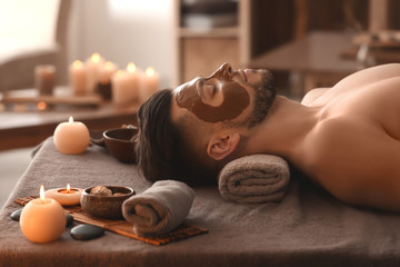 Young man with face mask on massage table in spa salon