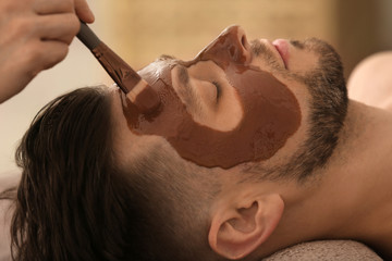 Naklejka premium Beautician applying cosmetic mask on man's face in spa salon