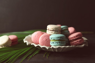 Plate with tasty macarons and palm leaves on table