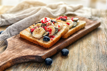 Tasty sweet toasts with fresh sliced banana and berries on wooden board
