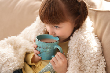 Cute little girl with cup of hot cocoa drink at home