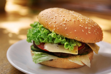 Plate with tasty cheeseburger on table
