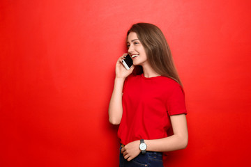 Beautiful young woman talking on mobile phone against color background