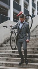 Handsome young adult man wearing suit holding his classic bicycle on the shoulder while walking downstairs