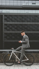 Handsome young adult man wearing suit checking phone before riding his classic bicycle to work in the morning