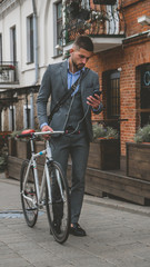 Handsome young adult man wearing suit choosing music on his phonee before riding his classic bicycle to work in the morning